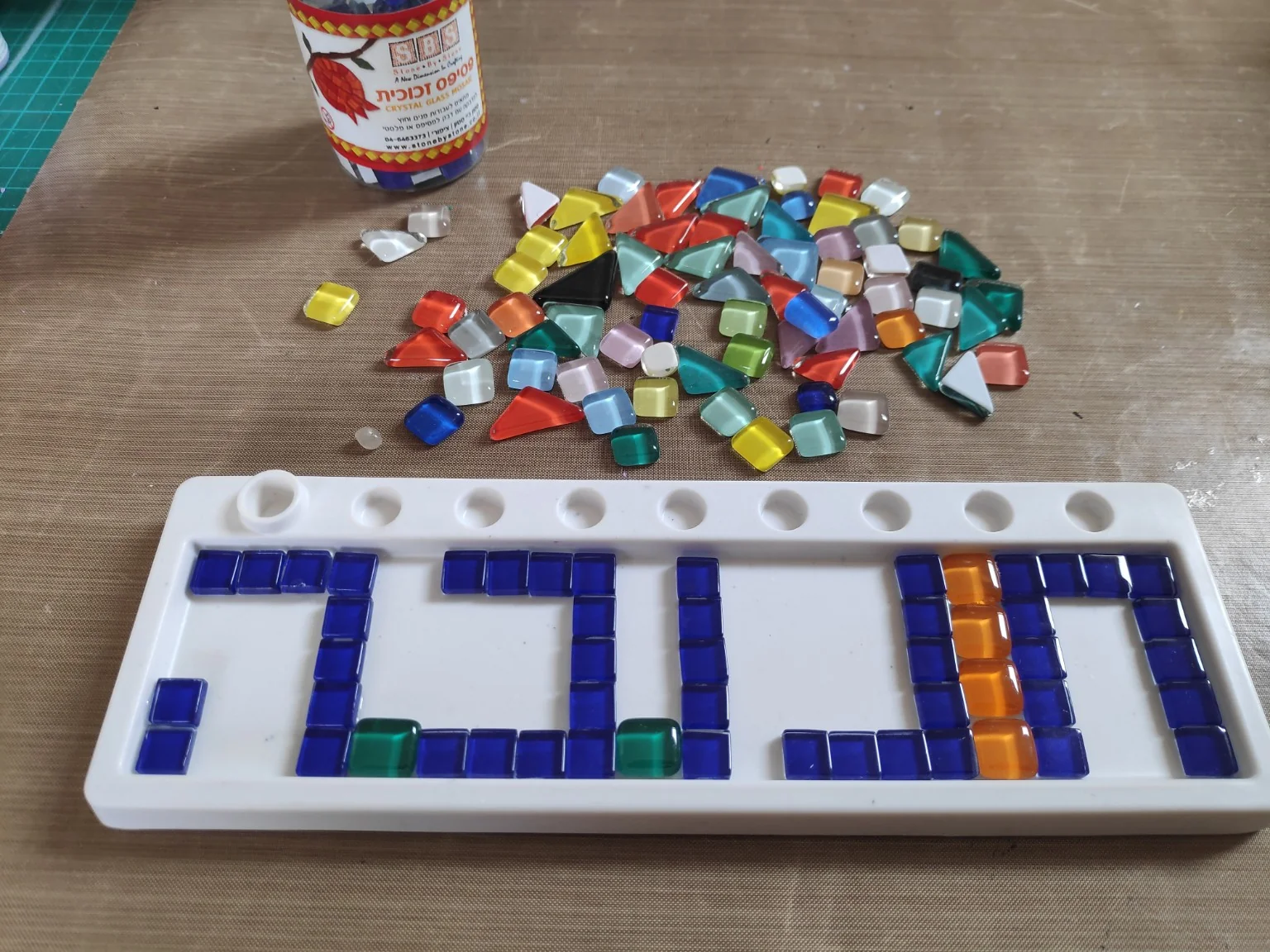 סידור אבני פסיפס כחולות ליצירת כיתוב על מגש החנוכייה